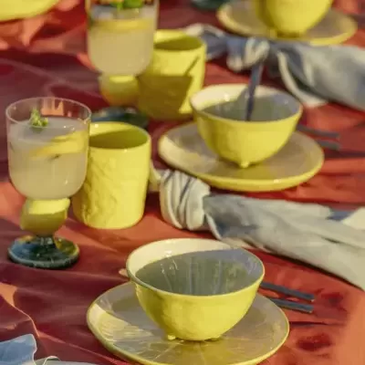 Conjunto de loiça amarela com textura irregular em mesa vermelha com guardanapos cinzentos