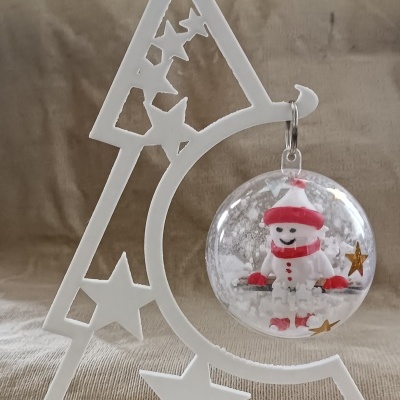 Suporte branco em formato de árvore com enfeite transparente e figura festiva no interior.