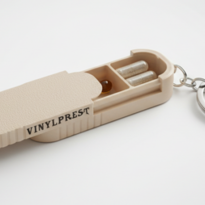 Chaveiro de plástico bege com texto VINYLPREST e cápsulas em compartimentos