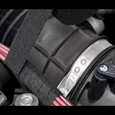 Componentes de motor automóvel com tubo plástico preto, braçadeira metálica com número '00' e cabos vermelhos protegidos por cinta preta