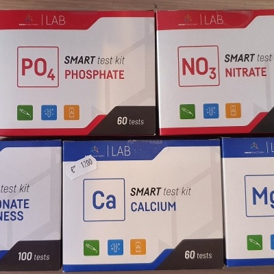 Cinco kits para análise de água, com rótulos para fosfato, nitrato, dureza do carbonato, cálcio e magnésio, sobre superfície de madeira