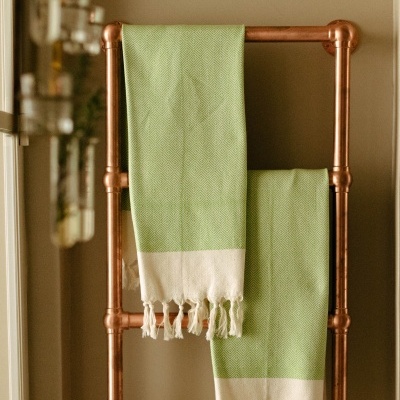 Toalhas verdes com franjas brancas penduradas em estrutura metálica cobre