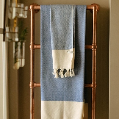 Toalha azul e branca com franjas pendurada em suporte metálico cor cobre