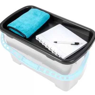 Tabuleiro preto com pano azul, caderno e caneta dentro de balde branco com alça azul