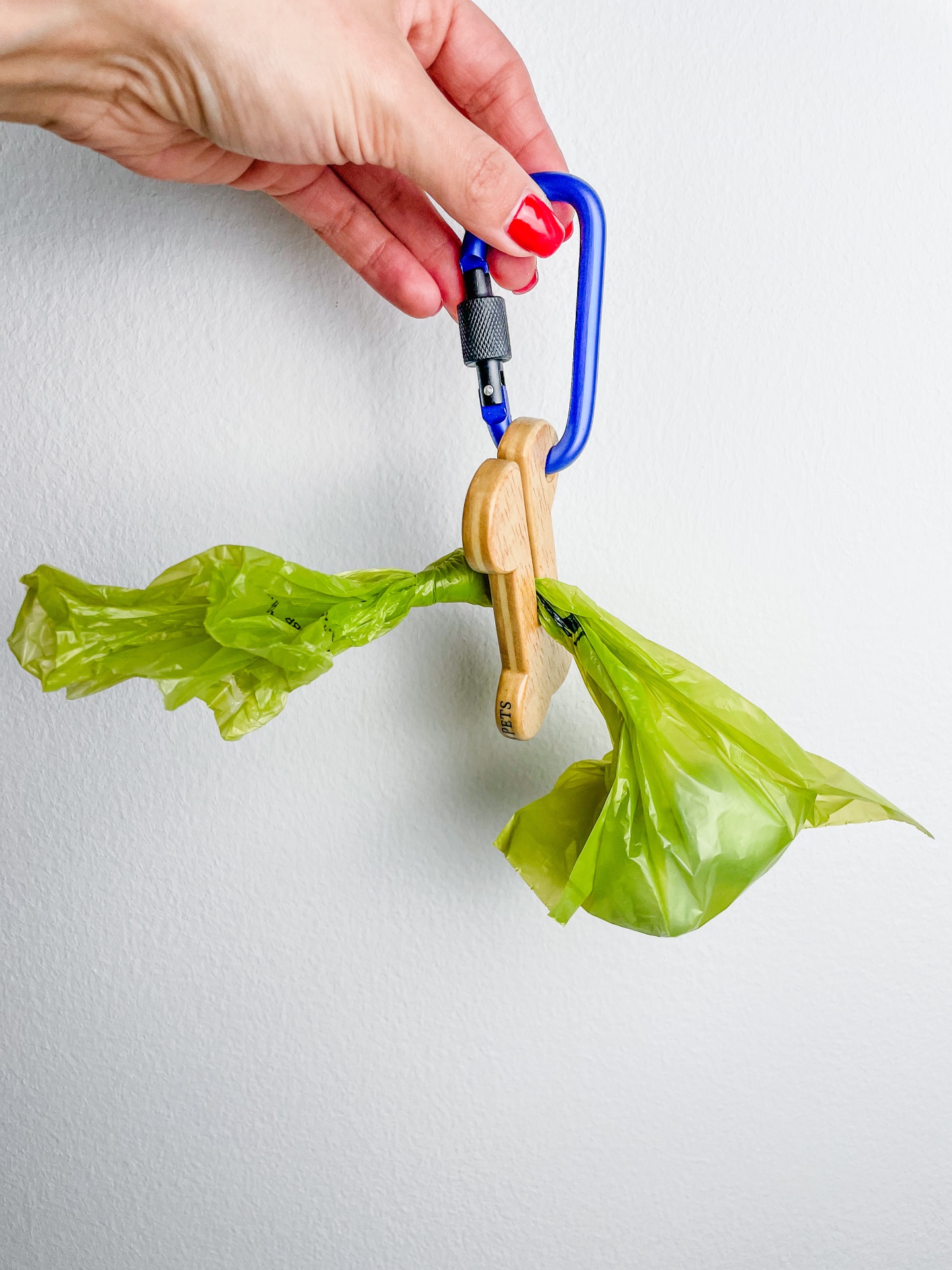 Mão segurando saquinhos verdes presos por prendedor de madeira com mosquetão azul