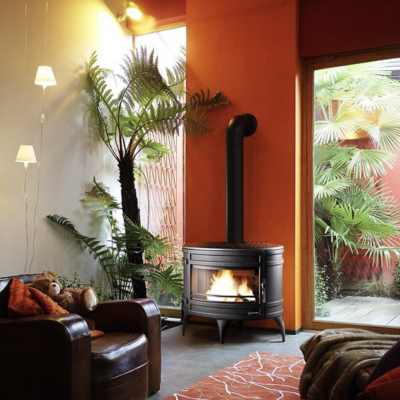 Sala de estar com lareira preta, sofá de couro, plantas e parede laranja