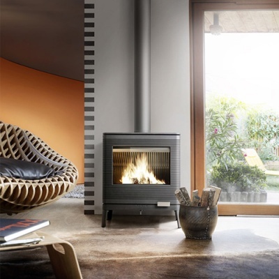 Lareira a lenha preta ligada no interior com cadeira de madeira clara e almofada preta perto de parede laranja e janela grande