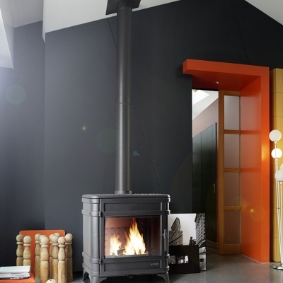 Lareira preta de ferro fundido acesa junto a objetos de madeira e porta com moldura laranja