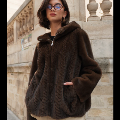 Casaco castanho peludo com capuz, mulher com óculos, ambiente urbano de pedra