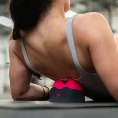 Dispositivo de massagem rosa e preto junto das costas de mulher em ginásio