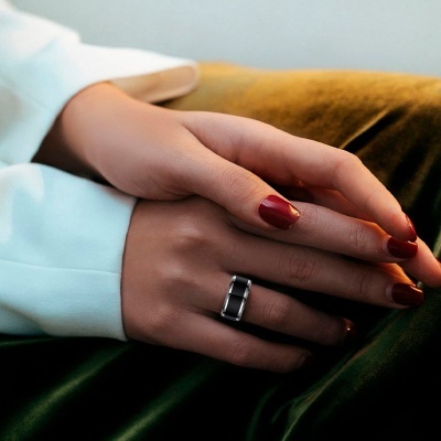 Mãos femininas com anel prateado e unhas vermelhas sobre tecido de veludo verde e castanho