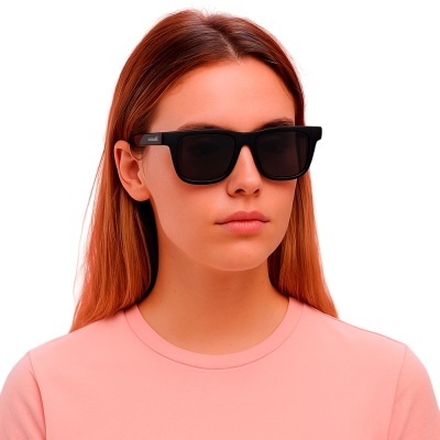 Mulher com óculos de sol preta e t-shirt rosa em fundo branco