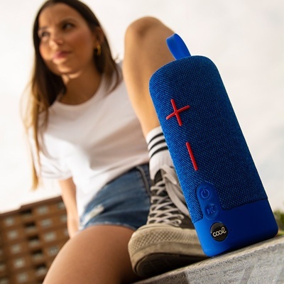 Coluna portátil azul com botões vermelhos em primeiro plano e jovem sentada ao fundo