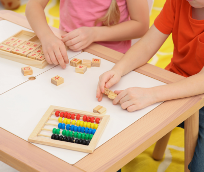 Duas crianças brincam com blocos de madeira com letras e um ábaco colorido numa mesa