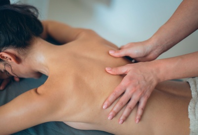 Pessoa a receber massagem nas costas com mãos visíveis numa sala interior