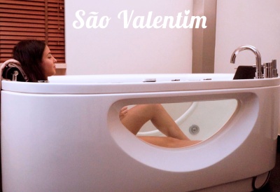 Banheira branca oval moderna com janela transparente lateral e mulher relaxando dentro.