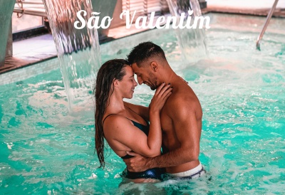 Casal na piscina abraçado com cascata de água ao fundo e texto São Valentim