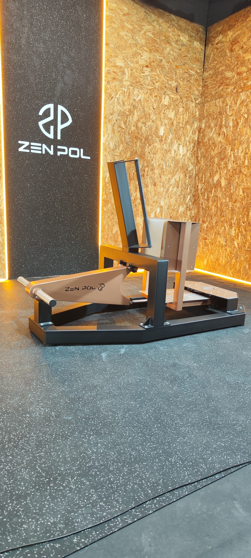 Máquina de exercício Zen Pol com estrutura preto e bege em chão com borracha preta e parede de madeira