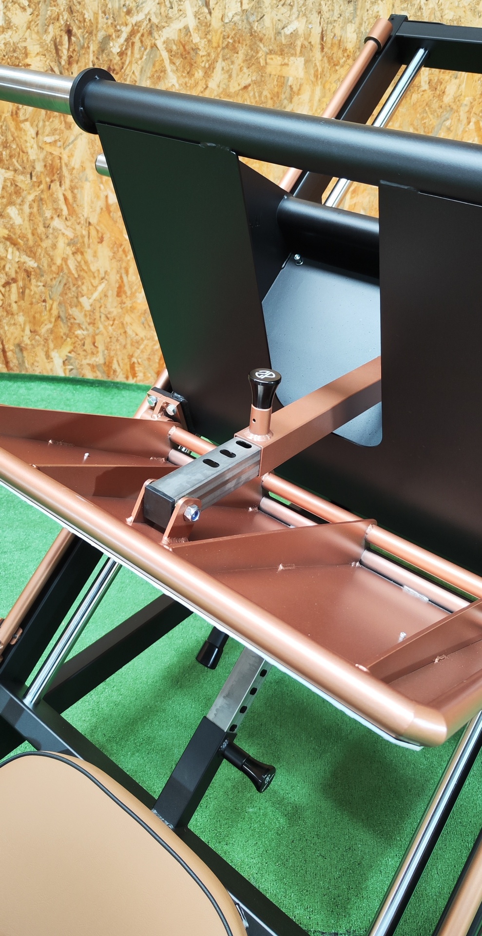 Aparelho de ginásio com estrutura metálica, assento bege e painel de madeira