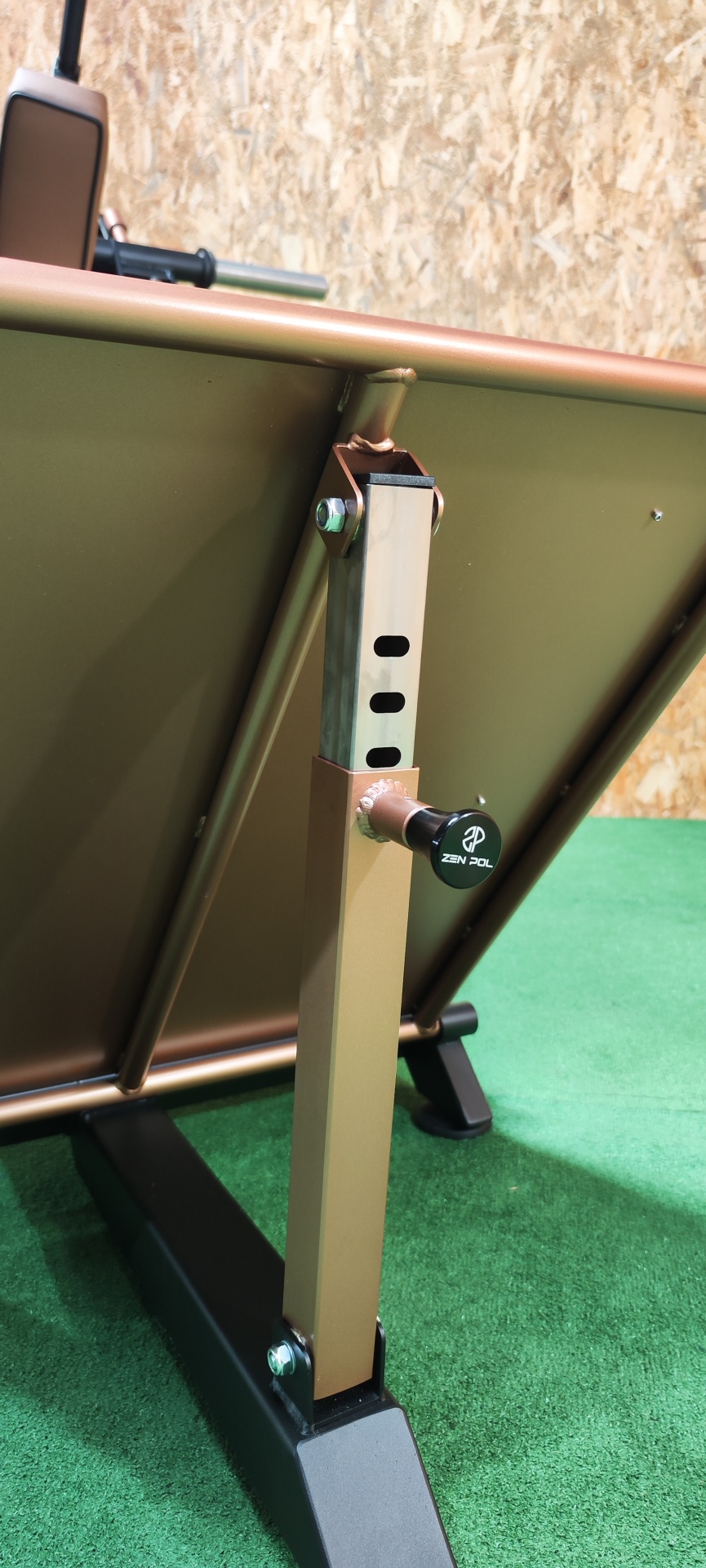 Pé ajustável de metal castanho com regulador preto ZEN POL em estrutura metálica castanha sobre base preta em carpete verde