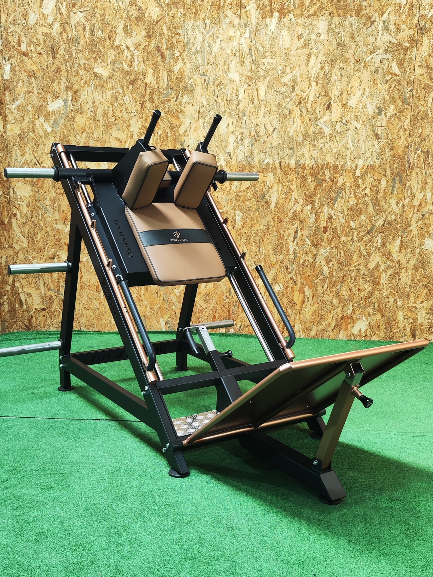 Equipamento de ginásio para treino de pernas preto e castanho num chão verde