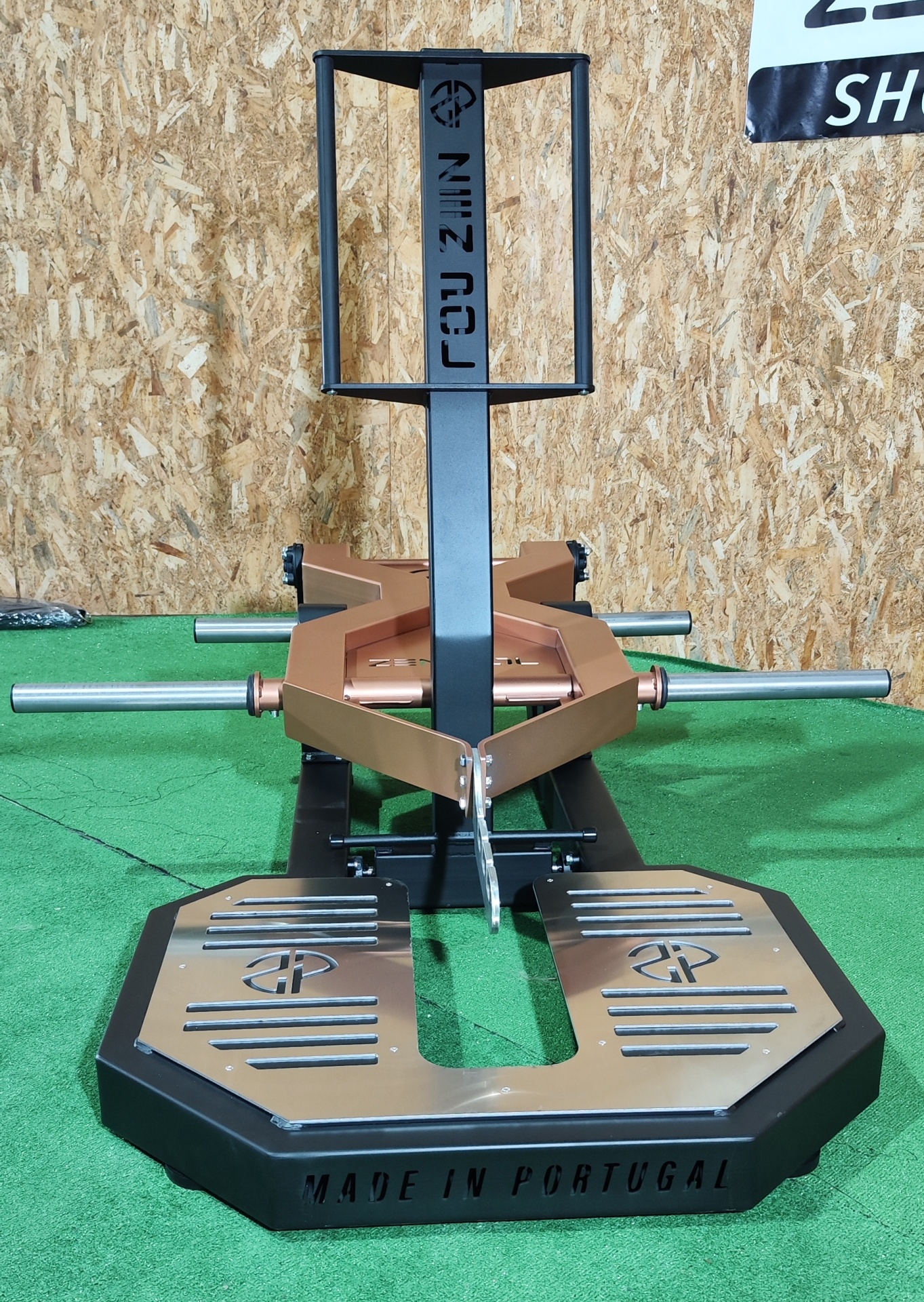 Equipamento de exercício metálico preto e dourado com texto 'FOCUSIN' e 'MADE IN PORTUGAL' em chão verde e parede de madeira