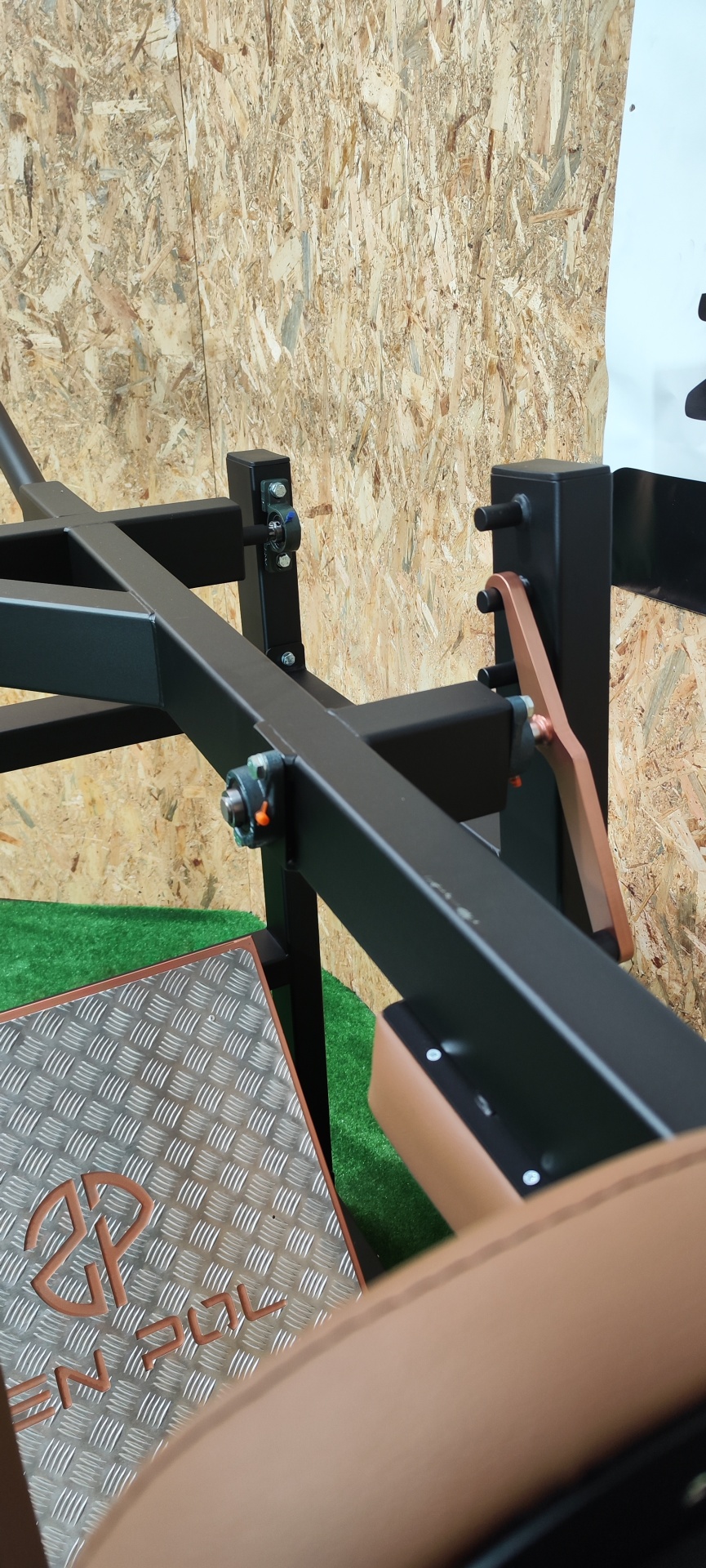 Máquina de exercício com almofadas castanhas e estrutura preta junto a uma parede de madeira aglomerada