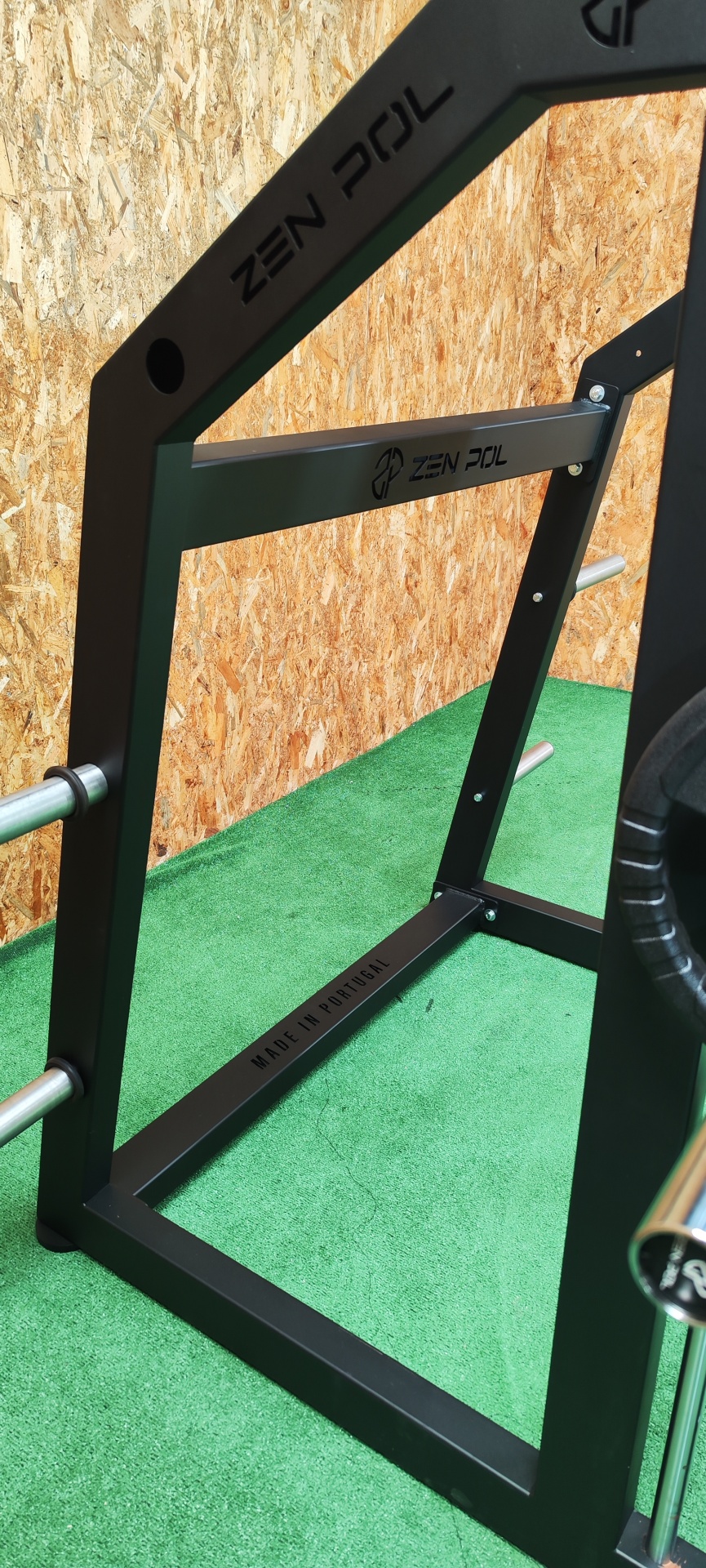 Estrutura metálica preta para suporte de pesos com etiquetas 'ZEN POL' e 'MADE IN PORTUGAL' sobre tapete verde