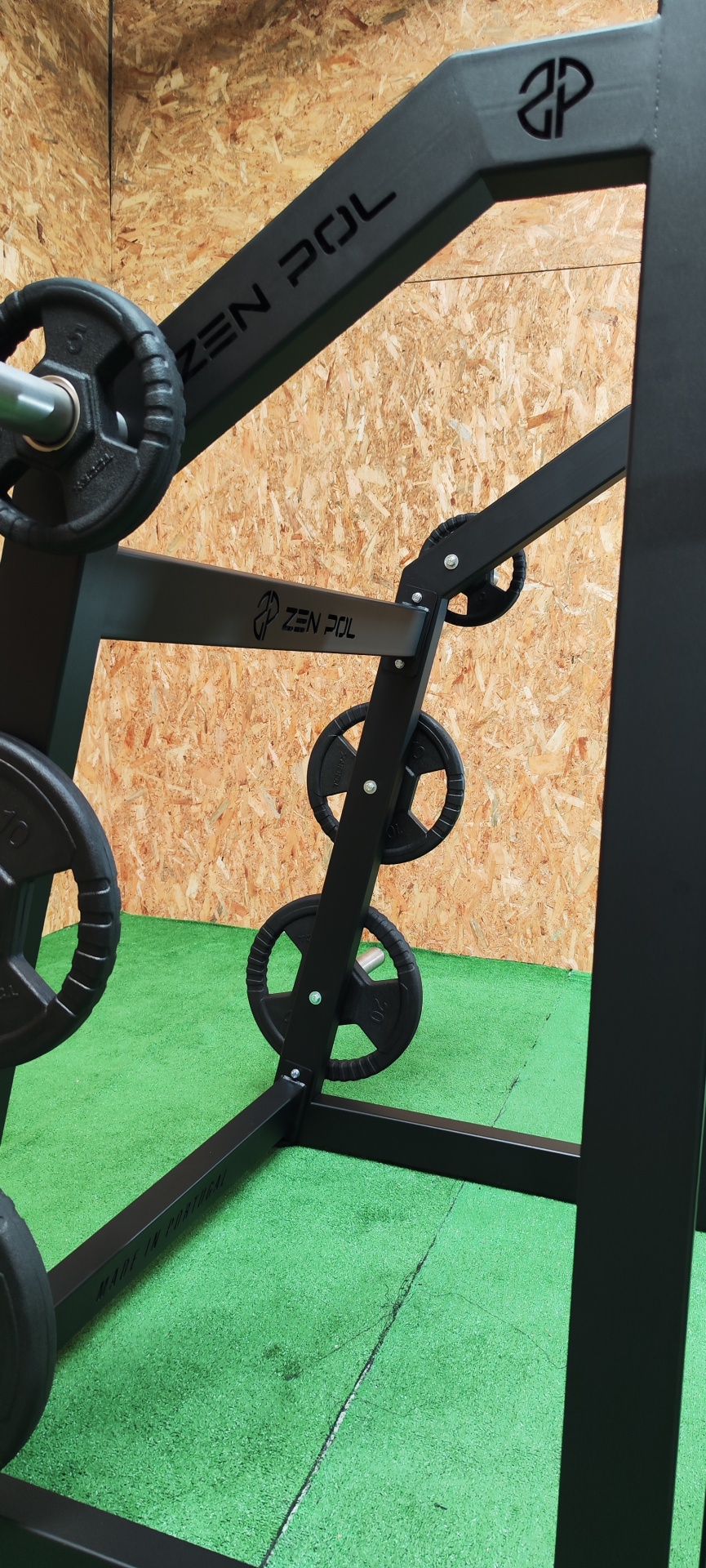 Suporte para pesos preto com placas redondas em chão verde e parede de madeira.