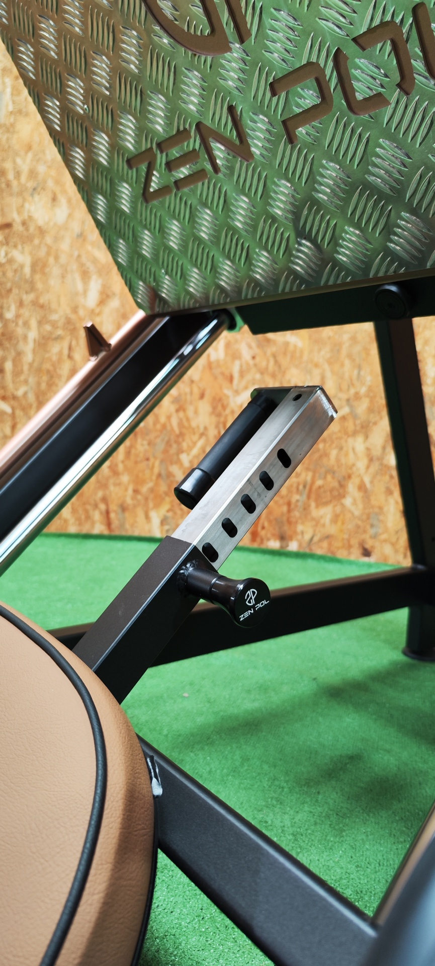 Detalhe de aparelho de fitness hidráulico com assento em pele castanha, estrutura metálica preta e placa metálica ZEN ZONE