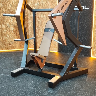 Máquina de treino de peito com acolchoamento bege e estrutura metálica preta e marron numa sala com piso antiderrapante.