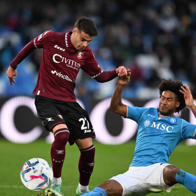 Dois jogadores de futebol em ação no campo, um com equipamento vermelho e outro azul